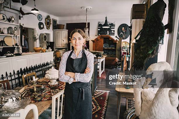 portrait of female retailer with arms crossed standing in antique shop - secondhand försäljning bildbanksfoton och bilder