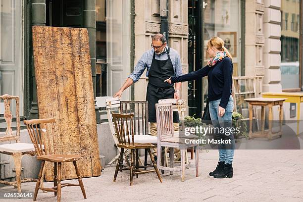 female costumer pointing while retailer looking at chair outside antique shop - antique shop stock pictures, royalty-free photos & images