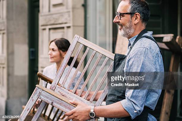 colleagues holding wooden chairs while standing outside antique shop - man in antique shop stock pictures, royalty-free photos & images