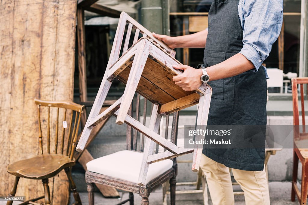 Midsection of man holding chair while standing against store