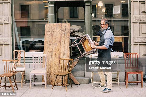 full length of man holding chair while arranging outside store - vintage furniture stockfoto's en -beelden