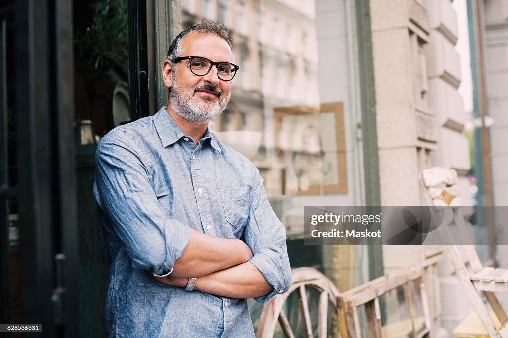 Portrait of owner standing with arms crossed outside antique shop