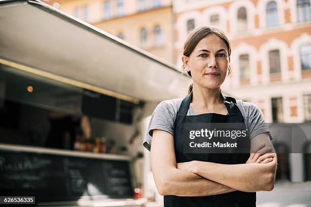 front view of confident female chef standing by food truck in city - apron lady stock-fotos und bilder