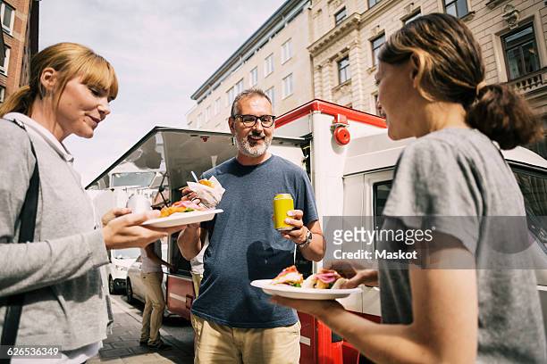 people eating snacks while standing against truck at city - food truck street stock pictures, royalty-free photos & images