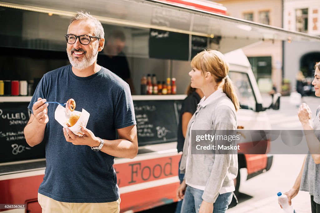 Mature man eating food while standing against truck at street