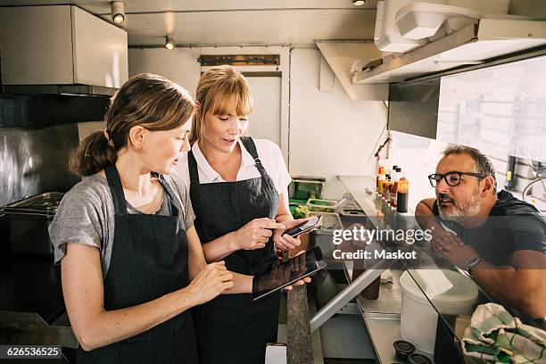 female chefs with technologies while receiving order from man in food truck - autonomo smartphone tablet fotografías e imágenes de stock