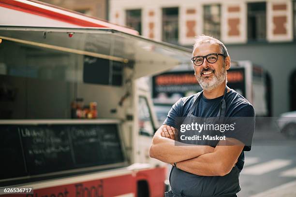 portrait of confident chef with arms crossed standing by food truck on street - furgone ambulante foto e immagini stock