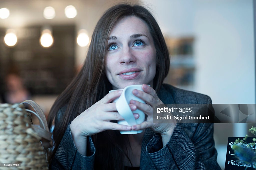 Young woman looking up whilst drinking coffee in cafe