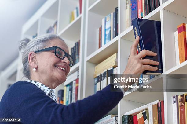 grey haired mature woman selecting book from bookshelves - shelf strip stock pictures, royalty-free photos & images