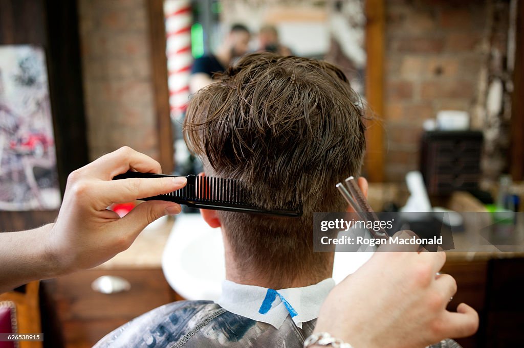 Rear view of young man in barbershop having haircut