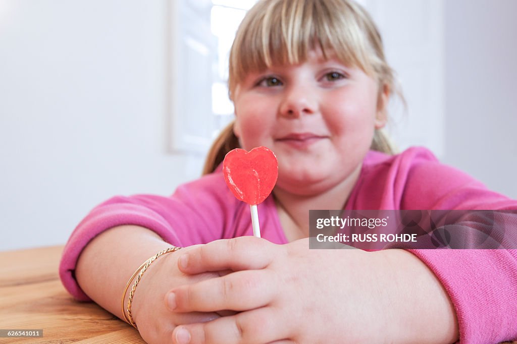 Portrait of overweight girl holding heart shape lollipop