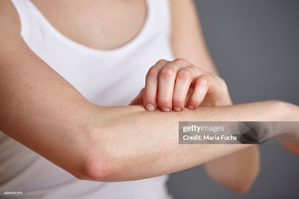 Cropped shot of young woman scratching her forearm with fingers