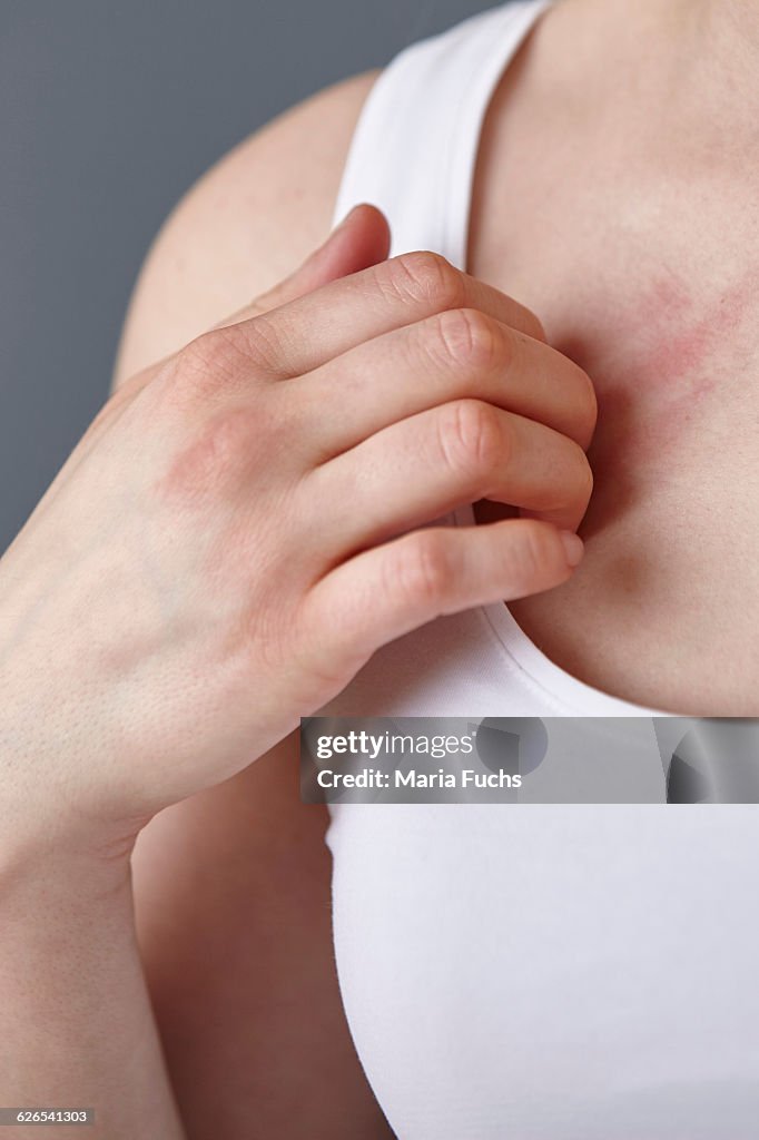 Cropped close up shot of young woman scratching her chest with fingers