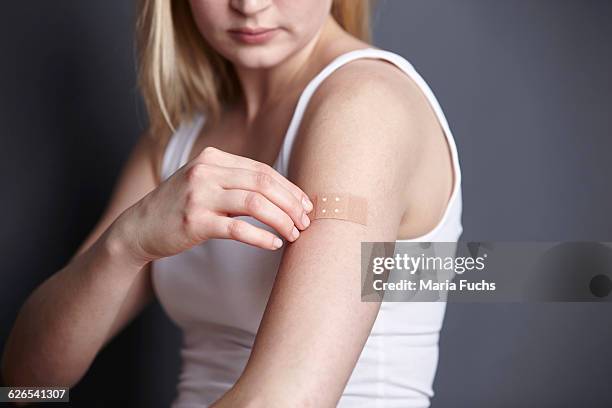 cropped shot of young woman applying adhesive plaster to her own arm - applying plaster stock pictures, royalty-free photos & images