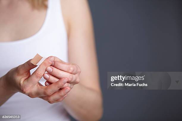 cropped close up shot of young woman applying adhesive plaster to her own finger - finger studio close up stock-fotos und bilder