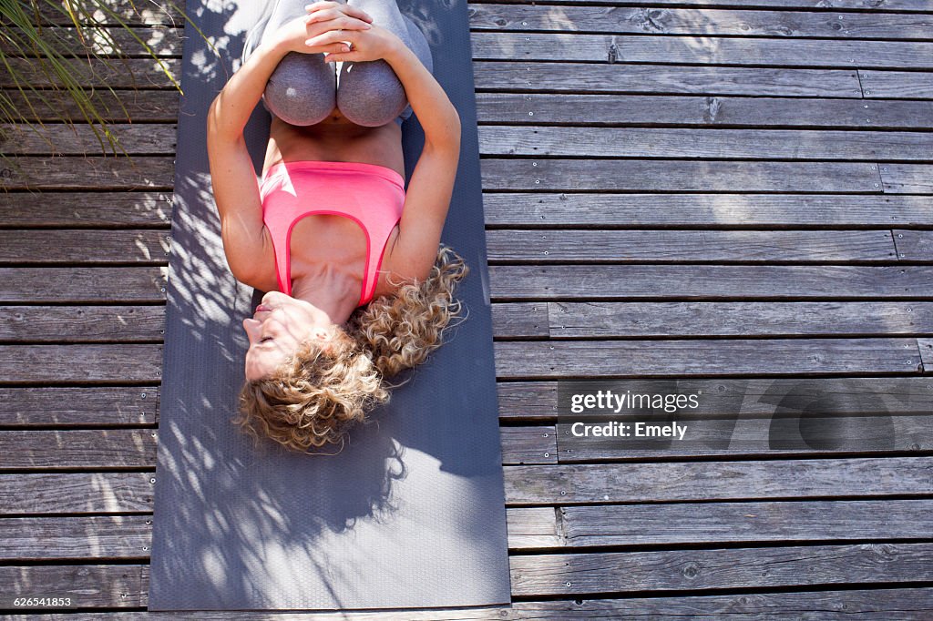 Young woman lying on yoga mat, hugging knees, high angle