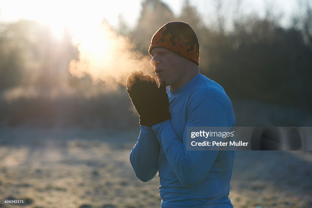 Runner wearing knit hat and gloves, rubbing hands together, breathing cold air