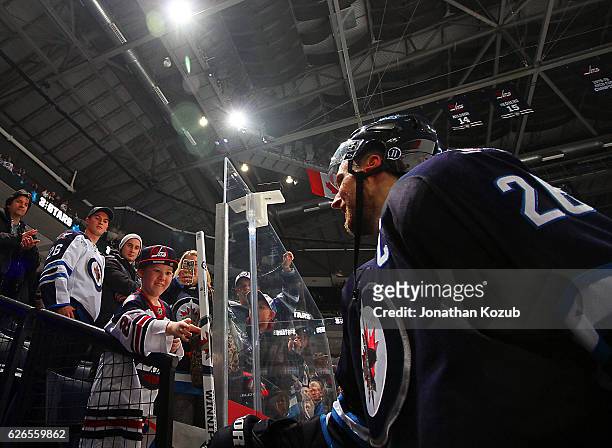 Blake Wheeler of the Winnipeg Jets hands a souvenir stick to a lucky fan after being named the first star of the game following a 3-2 victory over...