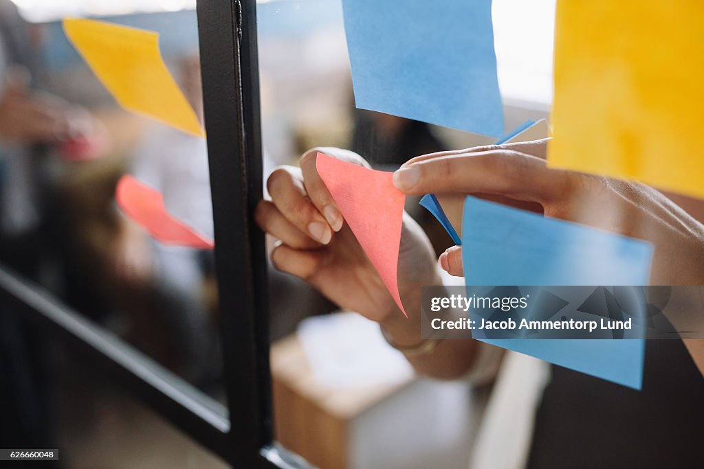 Hands of woman sticking adhesive notes on glass
