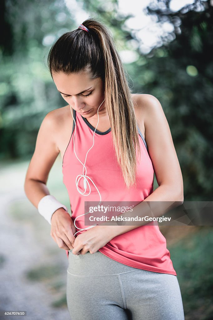 Sportlerin bereitet Musik auf dem Smartphone vor dem Training in der Natur vor