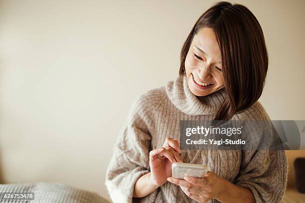 ベッドルームでスマートフォンを使用した中期成人女性 - 女性　日本人　笑顔　30代 ストックフォトと画像