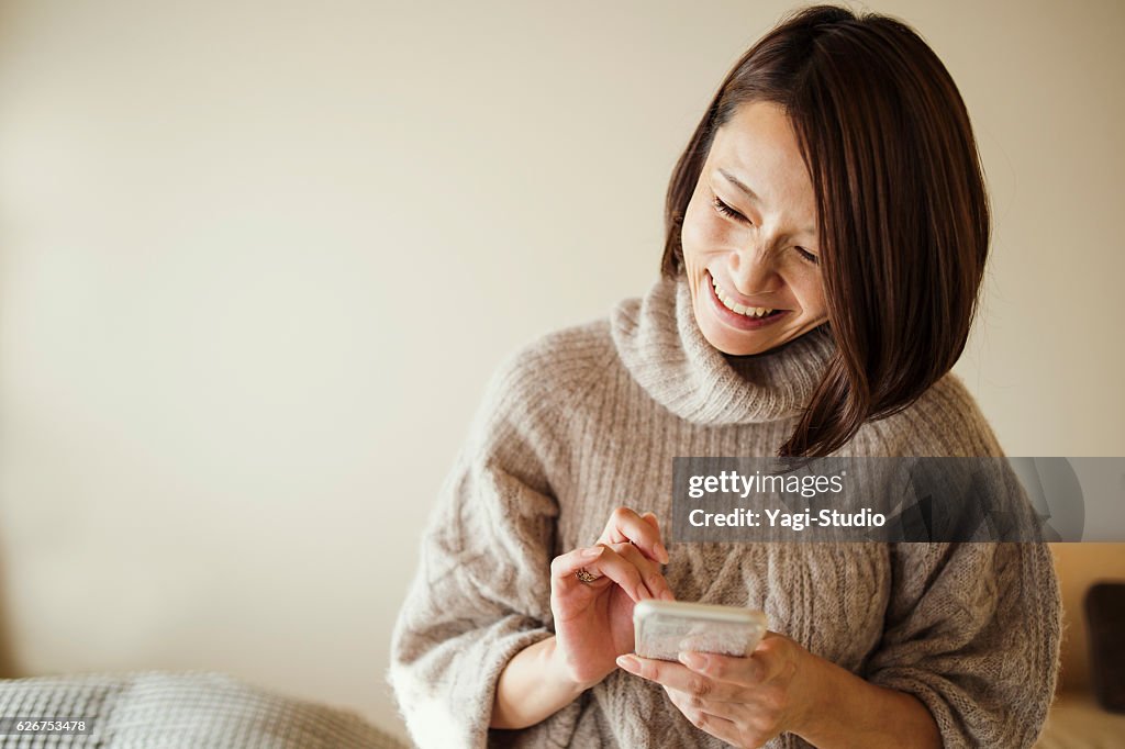 Mid adult woman using a smart phone in bed room