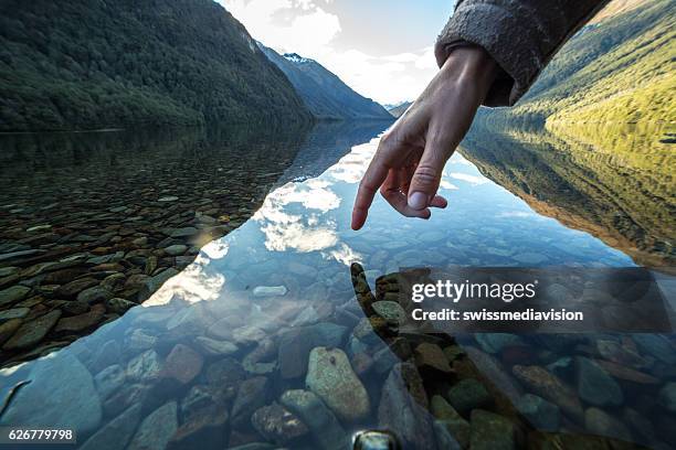 doigt touche la surface d'un lac de montagne, nouvelle-zélande - transparent photos et images de collection