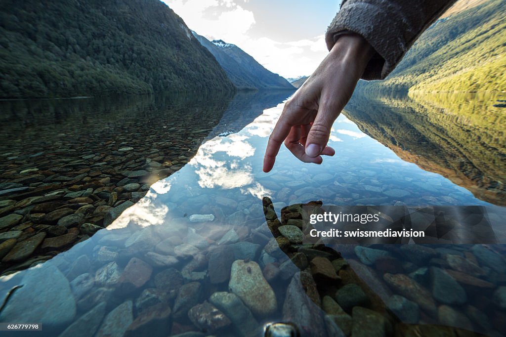 Finger touches surface of mountain lake, New Zealand