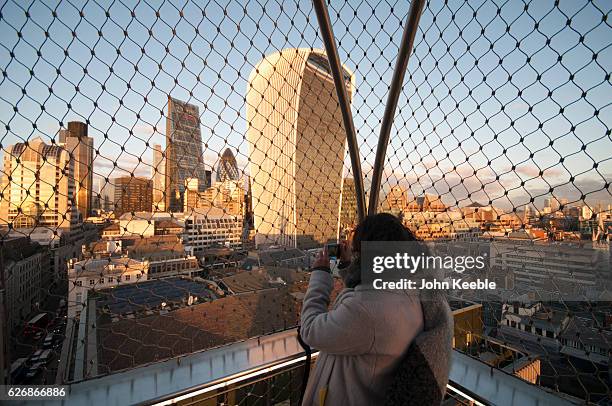 Tourists at the top of the Monument to the Great Fire of London look out and take pictures of the Walkie Talkie building as the sun sets on November...