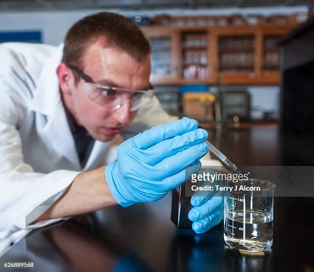 chemiker fügt schwefelsäure zu einem becher mit einem tropfen - sulfuric acid stock-fotos und bilder