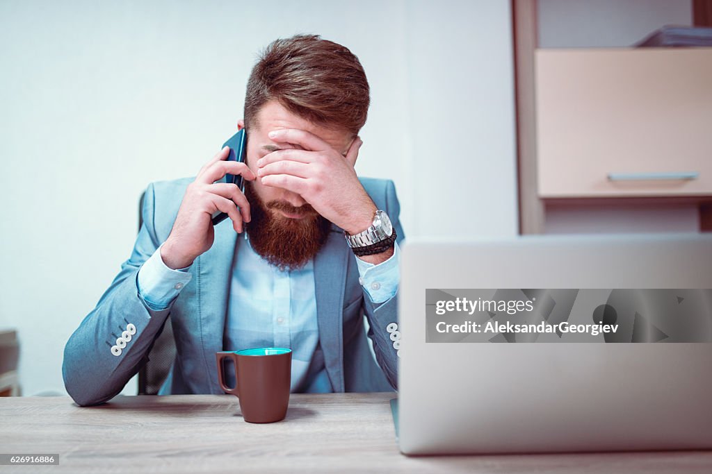 Empresario preocupado y agotado hablando por teléfono en su oficina