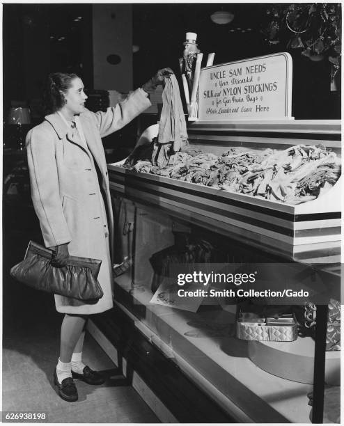 Part of a campaign to collect used nylon stockings for American efforts during World War II, a young woman holds up a pair of disbanded stockings...