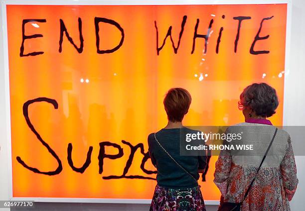 Art patrons look at Sam Durant's "End White Supremacy" during Art Basel in Miami on November 30, 2016. Art Basel represents over 250 art galleries at...