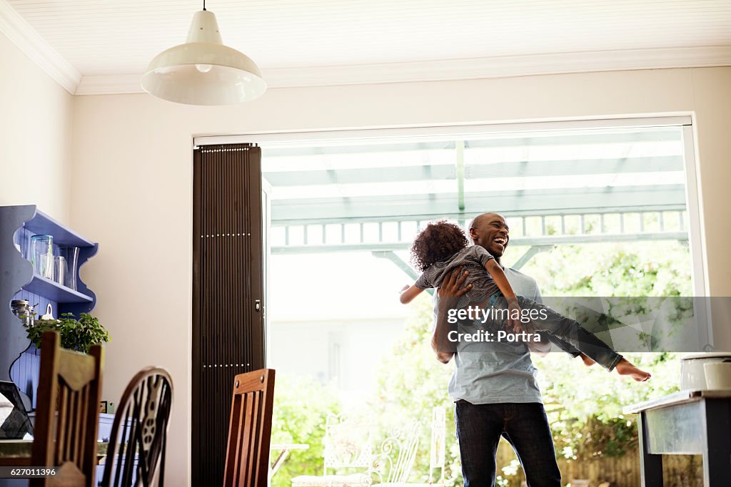 Cheerful man lifting boy at home