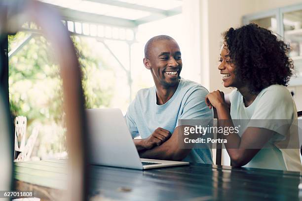 alegre casal usando o laptop em casa - african american couple - fotografias e filmes do acervo