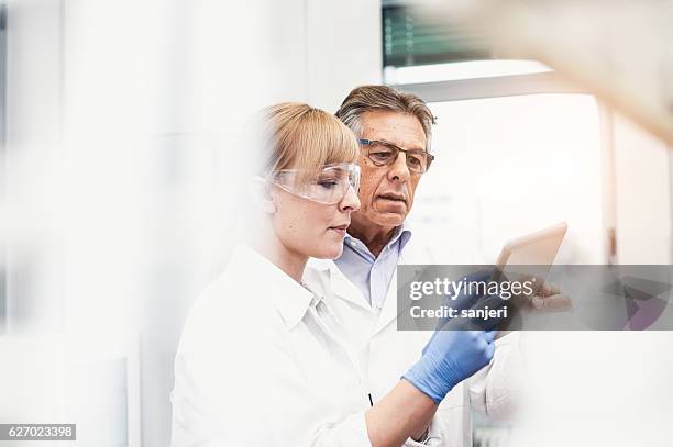 scientist discussing and using digital tablet - medisch laboratorium stockfoto's en -beelden