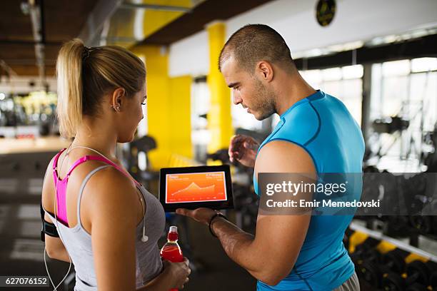 young woman discussing workout progress with fitness instructor - sport tablet stockfoto's en -beelden