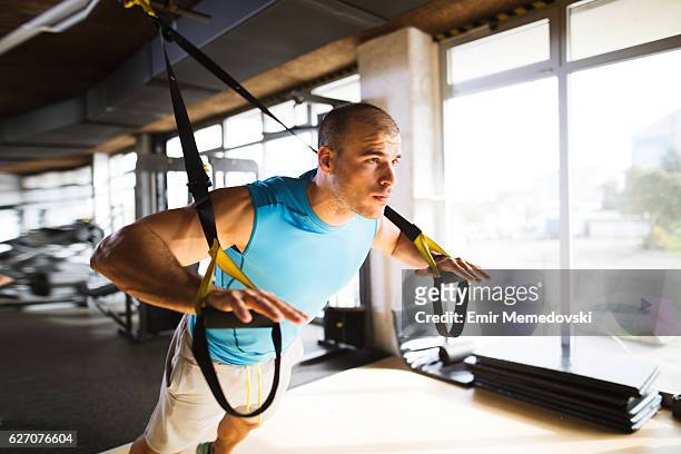 man doing arm exercises with suspension straps at gym - suspension training stock pictures, royalty-free photos & images