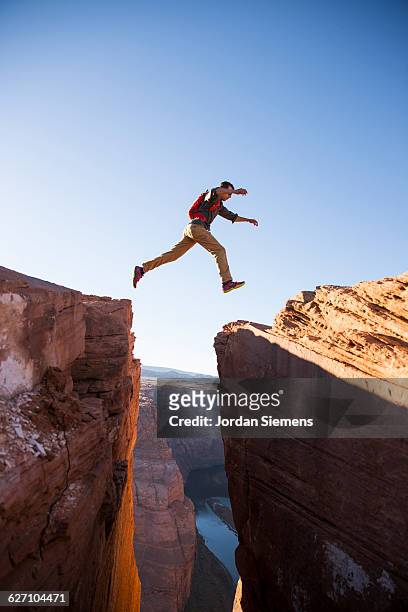 a man jumping between cliffs. - cliff side stock pictures, royalty-free photos & images