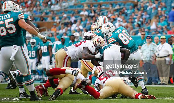 Nick Bellore and Ahmad Brooks of the San Francisco 49ers tackle Jay Ajayi of the Miami Dolphins during the game at Hard Rock Stadium on November 27,...