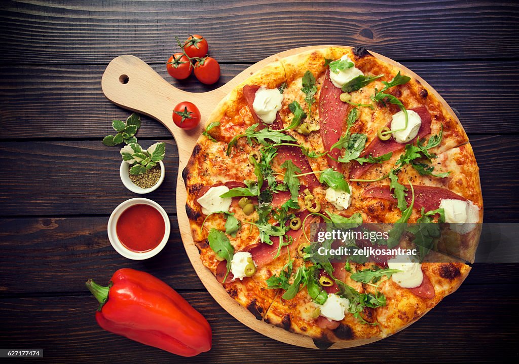 Rustic pizza with salami, olives and basil on wooden table