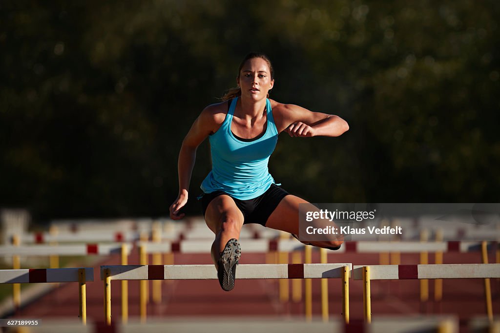 Female athelete jumping over hurdle at sunrise