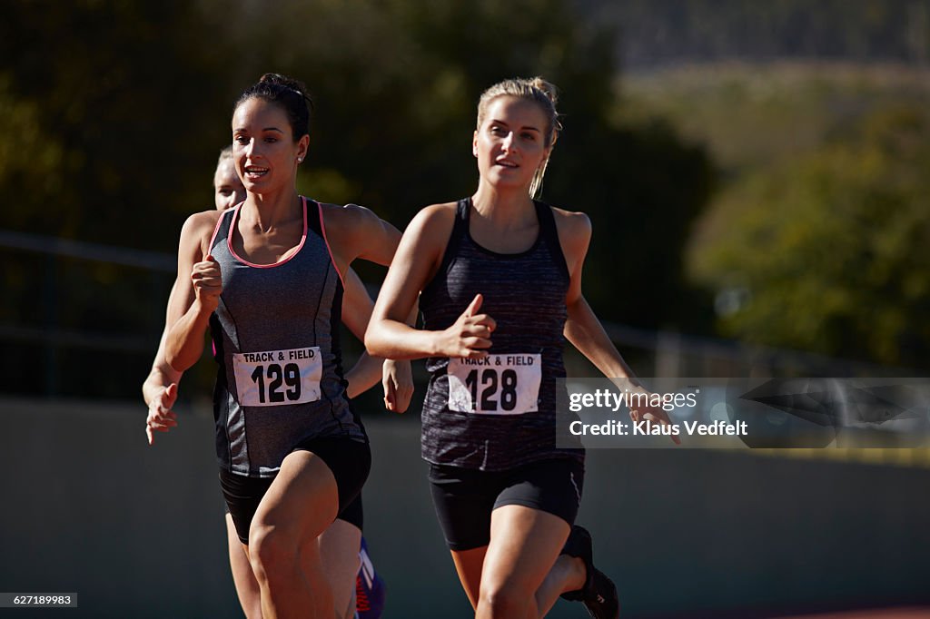 Female runnuers racing at stadium, close to finish