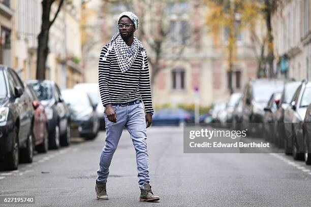 Sidya Sarr is wearing Zara blue denim slim jeans, Zara brown shoes, a Zara striped top, a Bomberg watch, a keffiyeh scarf, a blue belt, and a...