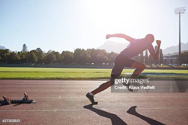 male athlete sprinting out of start block - mens track photos et images de collection