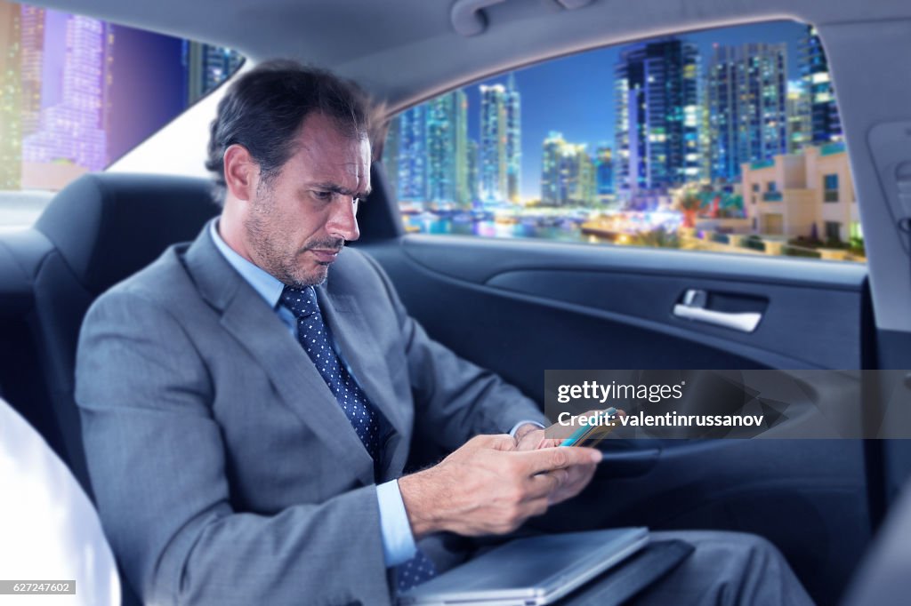 Frowning businessman traveling in car and using smart phone