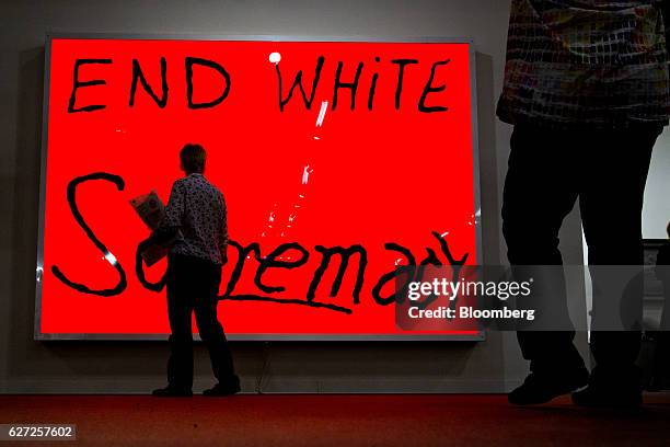 Visitors walk past the artwork "End White Supremacy" by Sam Durant on display during Art Basel Miami Beach in Miami, Florida, U.S., on Friday, Dec....
