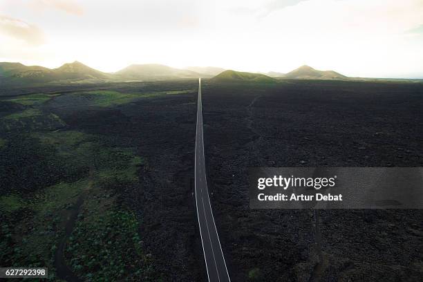 aerial picture taken with drone flying over the beautiful lanzarote island with volcano landscape and nice long straight road in the dark land with stunning sunset light. - long road stockfoto's en -beelden