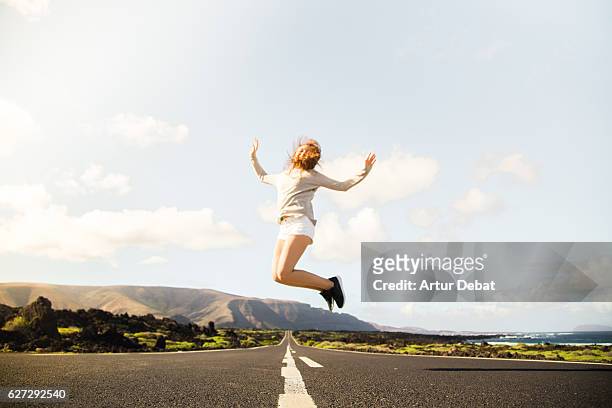 happy girl jumping on a beautiful long straight road in the volcanic island of lanzarote during a travel vacations. - mens long jump stockfoto's en -beelden