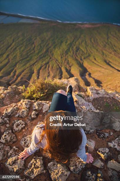 girl sitting and contemplating the volcanic island of lanzarote with nice sunset light from top of viewpoint during a travel vacations through the island. - vertigo stock pictures, royalty-free photos & images